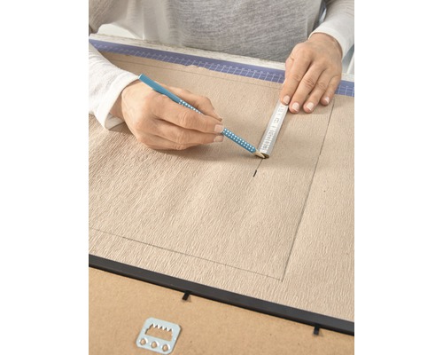 Een persoon tekent met potlood en liniaal op een canvas in een fotolijst.