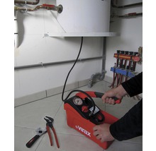 Een druktestpomp met manometer wordt bediend door een persoon, terwijl er een pijptang en moersleutel naast liggen.