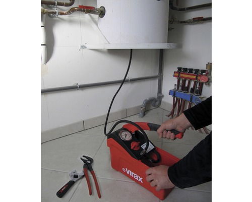 Een druktestpomp met manometer wordt bediend door een persoon, terwijl er een pijptang en moersleutel naast liggen.