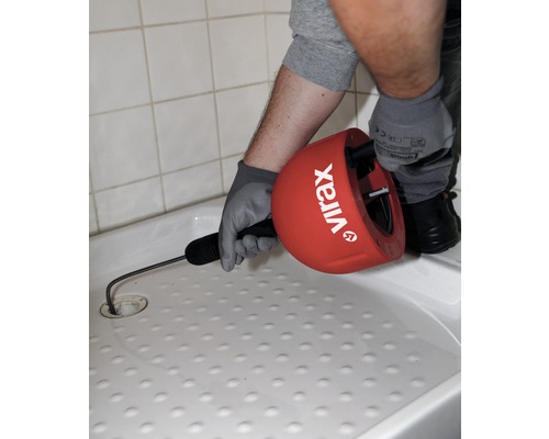 Een persoon gebruikt een ontstoppingsveer van het merk Virax in een douchebak om een verstopping te verwijderen.