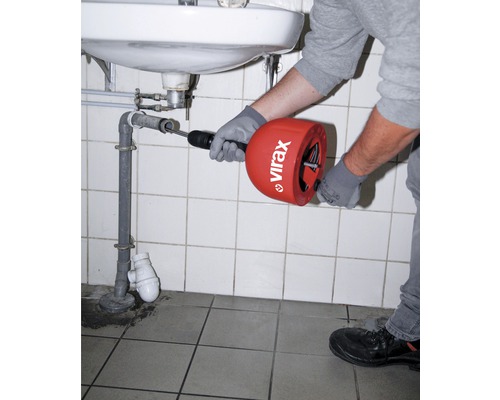 Iemand gebruikt een ontstoppingsveer onder een wastafel om een verstopping te verwijderen.