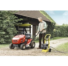 Een man bedient een Kärcher hogedrukreiniger naast een gazontractor in de tuin.