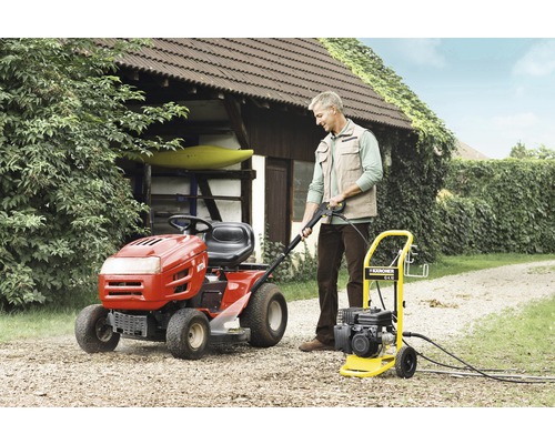 Een man bedient een Kärcher hogedrukreiniger naast een gazontractor in de tuin.
