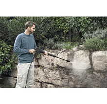 Man reinigt stenen muur met een hogedrukreiniger in de tuin.