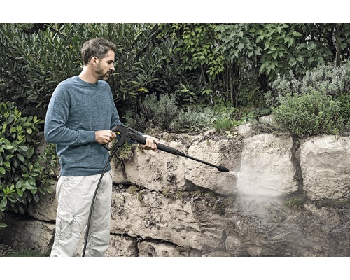Man reinigt stenen muur met een hogedrukreiniger in de tuin.