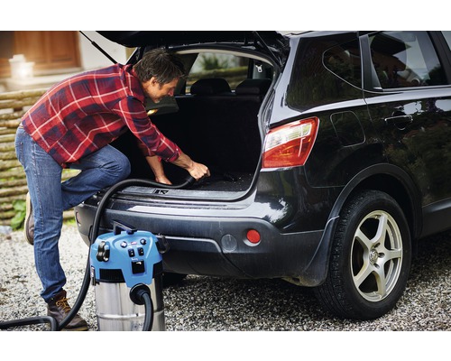 Een man stofzuigt de kofferbak van een auto met een nat- en droogzuiger.