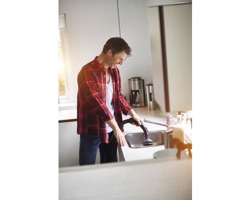 Een man maakt een gootsteen schoon met een stofzuiger in een lichte keuken.