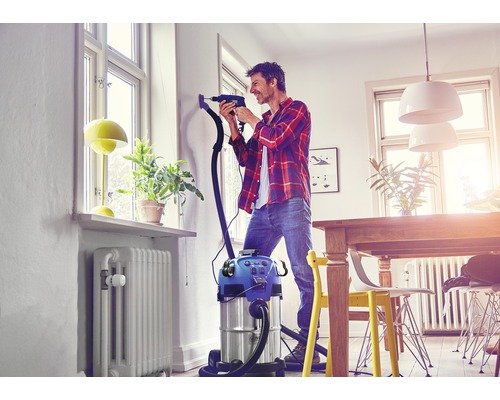 Man boort met stofzuiger in een helder appartement een gat in de muur