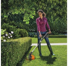 Vrouw snoeit heg met een grastrimmer in de tuin.