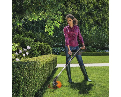 Vrouw snoeit heg met een grastrimmer in de tuin.
