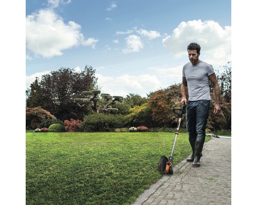 Een man gebruikt een gazonkantsnijder in de tuin om de rand van het gazon bij te werken.