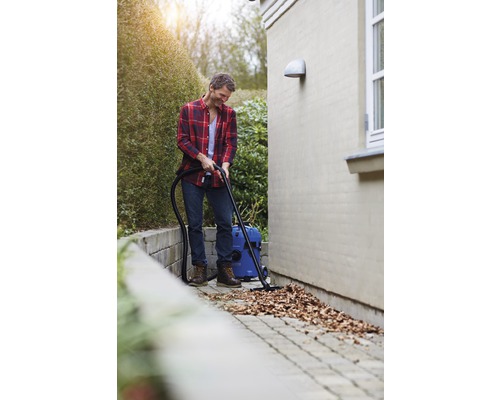 Een man zuigt bladeren op van een bestrating met een nat- en droogzuiger.