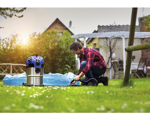Een man gebruikt een nat- en droogzuiger om een zwembad schoon te maken dat zich in de tuin bevindt.
