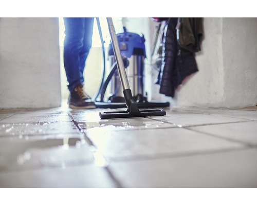 Iemand maakt een betegelde vloer schoon met een nat- en droogzuiger.