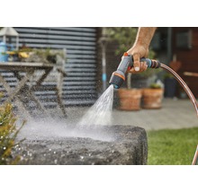 Persoon besproeit steen met een tuindouche en een tuinslang.