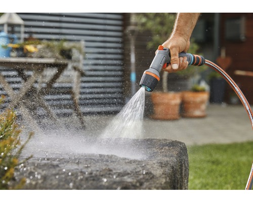 Persoon besproeit steen met een tuindouche en een tuinslang.