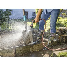 Een persoon reinigt een tuinschep met een tuinslang.