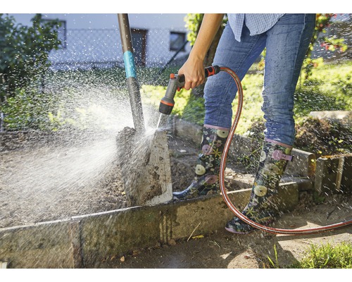 Een persoon reinigt een tuinschep met een tuinslang.
