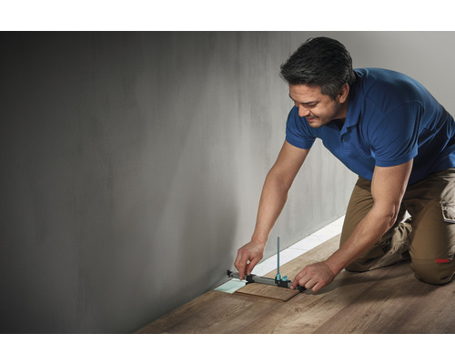 Een man gebruikt een aftekeninstrument om een stuk laminaat tegen een muur af te meten.