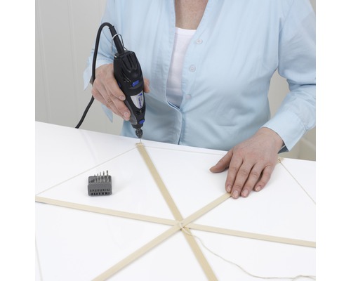 Een persoon boort met een Dremel multifunctioneel gereedschap een houten model.