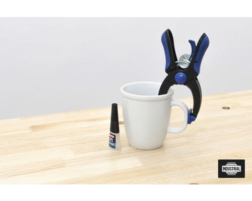 Een veerbelaste klem, een beker en een fles lijm op een werkbank