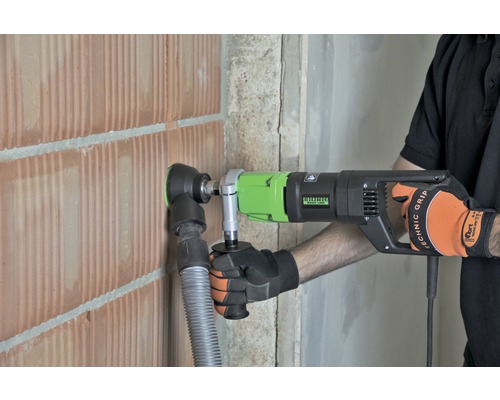 Een man boort met een kernboormachine een gat in een bakstenen muur.