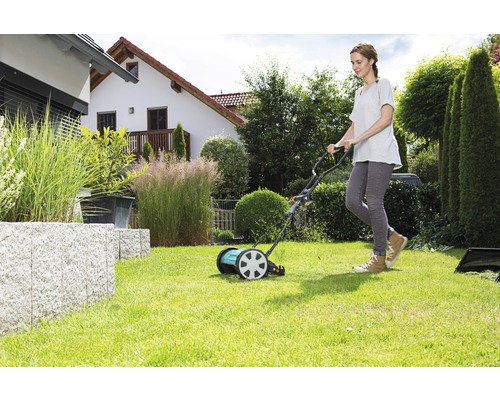 Vrouw gebruikt een handgrasmaaier in de tuin.