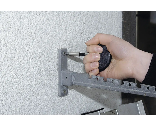 Een persoon bevestigt een metalen wasrek aan een muur met een schroevendraaier.