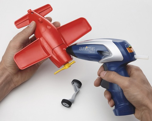 Persoon gebruikt een lijmpistool om een rood speelgoedvliegtuig te repareren