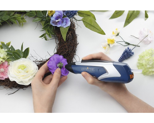 Vrouw bevestigt decoraties met een lijmpistool op een krans