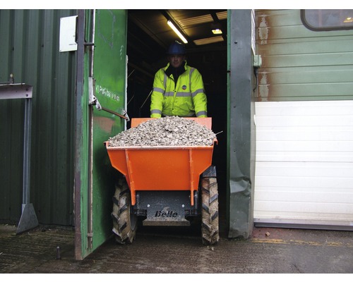 Een man vervoert grind met een dumper uit een gebouw.