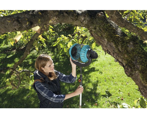 Vrouw gebruikt fruitverzamelaar in de tuin onder een boom.