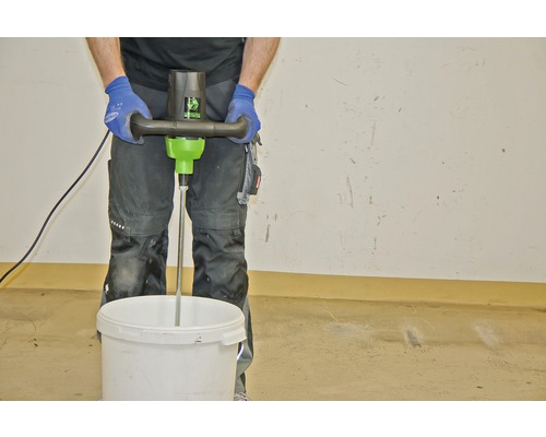 Ambachtsman mengt materiaal met een elektrische mixer in een emmer.