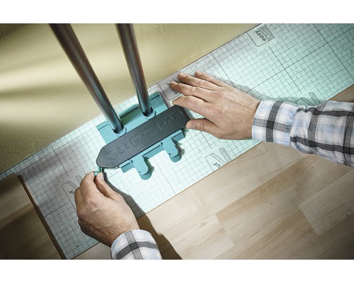 Wolfcraft Logo. Een persoon gebruikt een aftekenmal om verwarmingsbuizen af te tekenen op een isolerende onderlaag.