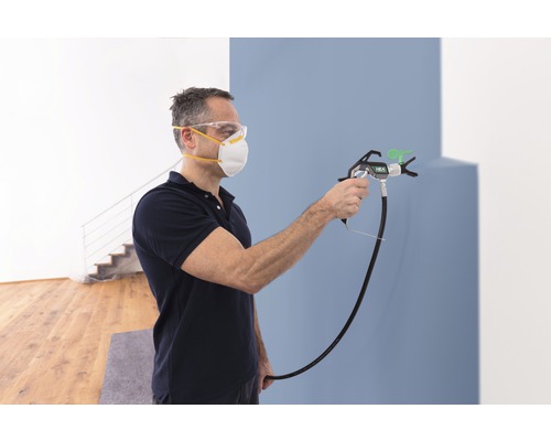Man schildert muur met verfspuit, hij draagt een veiligheidsmasker en een veiligheidsbril