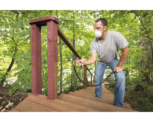 Man schildert houten buitentrap met een verfspuit