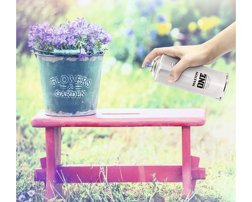 Scène met bloemen in een zinken emmer op een kruk, die wordt besproeid met een spuitbus verf.