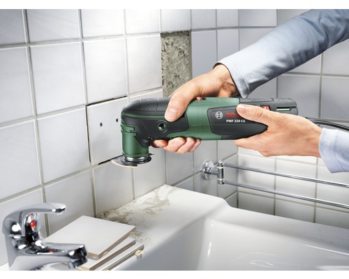 Een persoon gebruikt een Bosch multifunctioneel gereedschap om tegels te snijden.