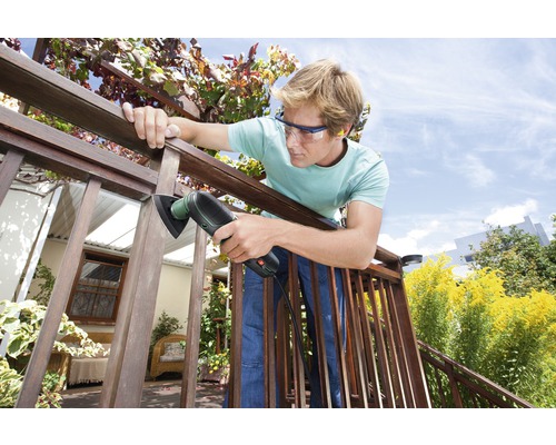 Man schuurt houten balustrade met een multischuurmachine buitenshuis. Hij draagt een veiligheidsbril.