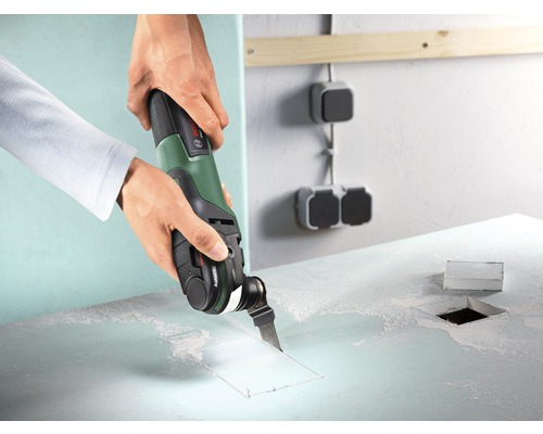 Ambachtsman snijdt met een multifunctioneel gereedschap een gat in een bouwplaat.