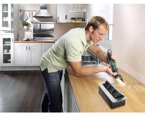 Man snijdt met een multifunctioneel gereedschap een gat in een keukenblad voor een stekkerdoos