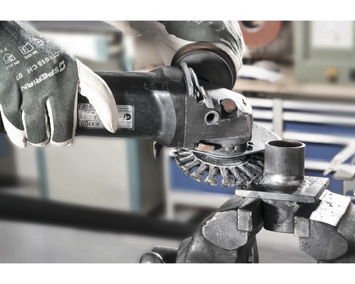 Een persoon gebruikt een draadborstel op een haakse slijper om een metalen onderdeel schoon te maken dat in een bankschroef is bevestigd.