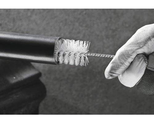 Een hand met een werkhandschoen reinigt een buis met een reinigingsborstel.