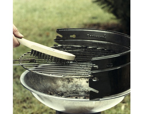 Een grillborstel met houten handvat reinigt een ronde houtskoolgrill.