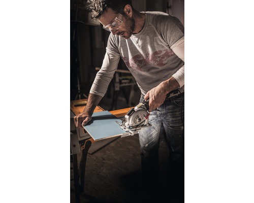 Een man met een veiligheidsbril snijdt een tegel met een handzaag.