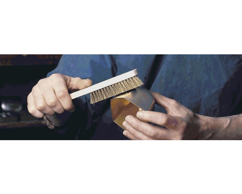 Een persoon reinigt een gouden voorwerp met een draadborstel.