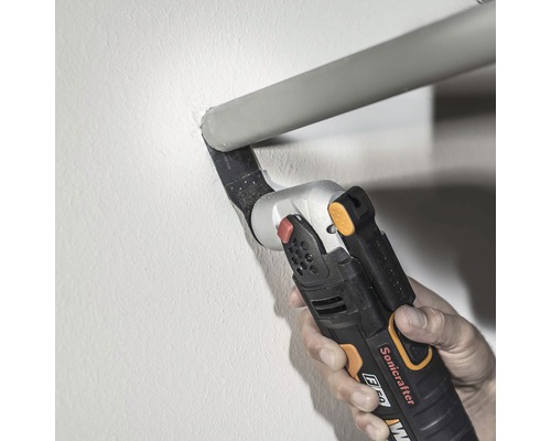 Een hand bedient een multifunctionele snijder om een buis aan een muur door te snijden.