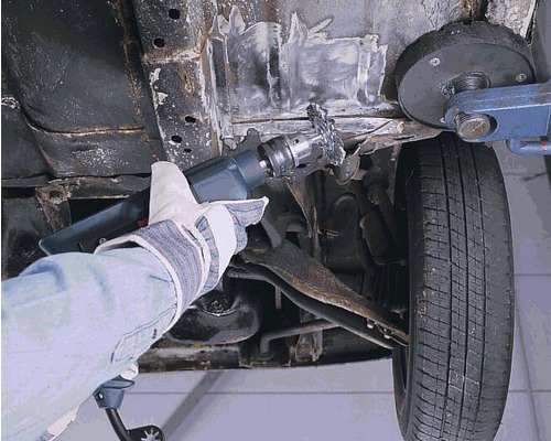 Een persoon verwijdert roest van een voertuig met een ontroestingsborstel.