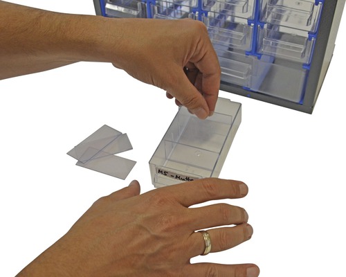 Een persoon vult een lade van een sorteerdoos met etiketten.