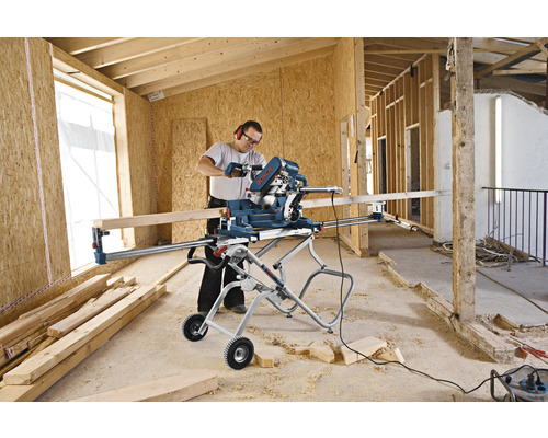 Een persoon gebruikt een Bosch verstekzaag op een montagestandaard in een onafgewerkte ruimte.